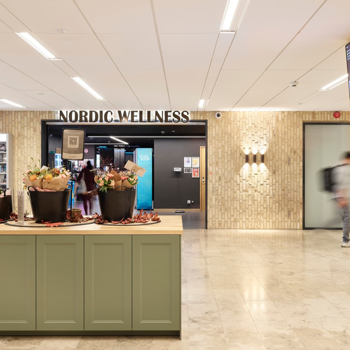 En person som går förbi en butiksfasad med blommor på disken.