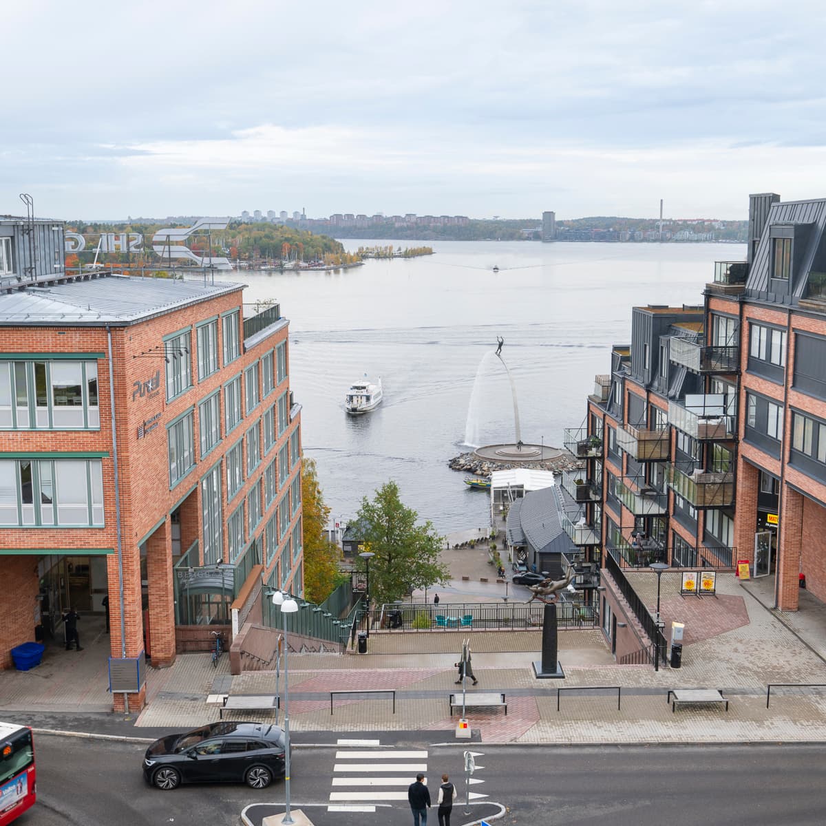 En röd buss kör längs en gata bredvid höga byggnader.