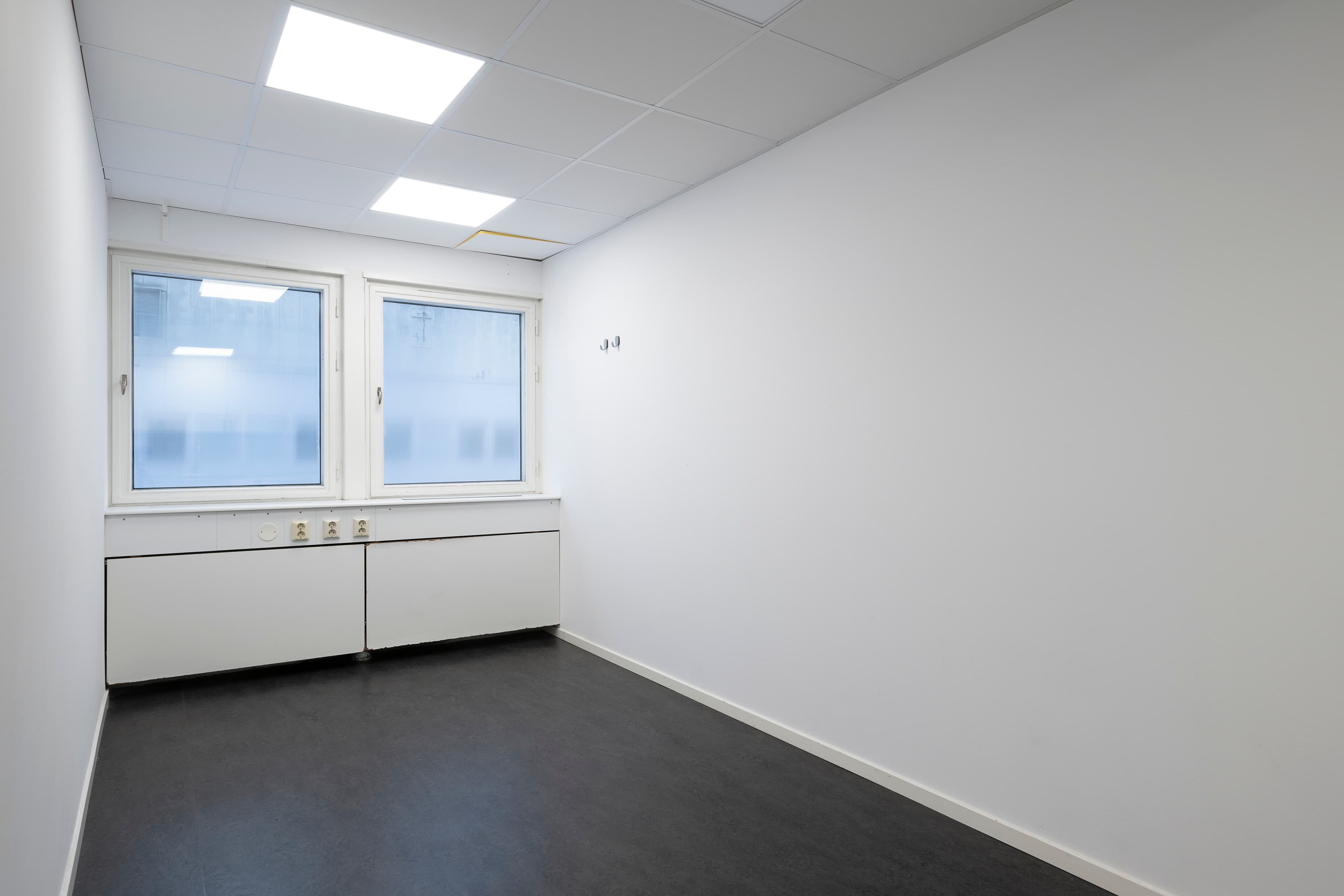 Ett tomt rum med vita väggar och fönster.