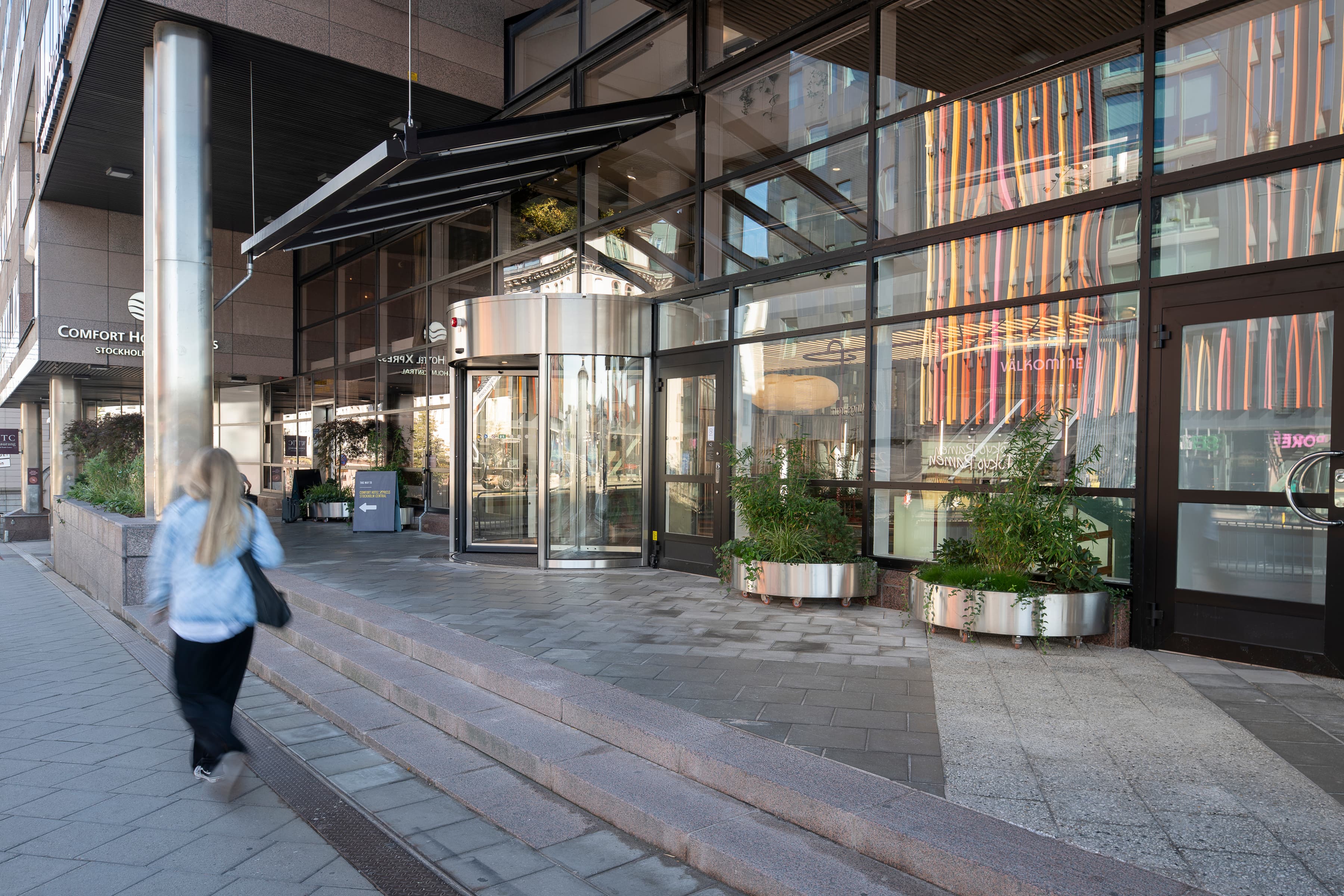 En kvinna går på en trottoar bredvid en hög byggnad.