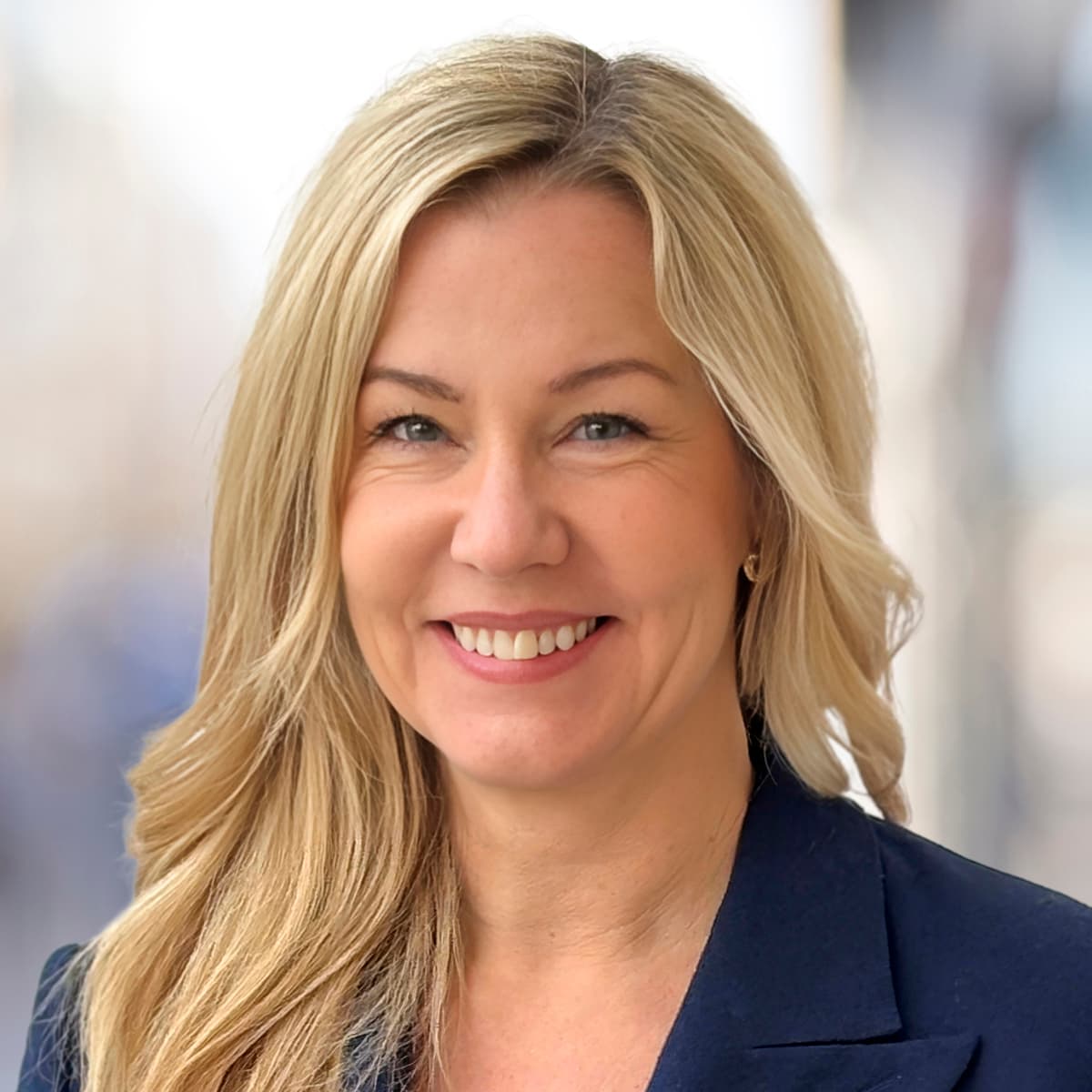 En kvinna i blå kavaj ler mot kameran.